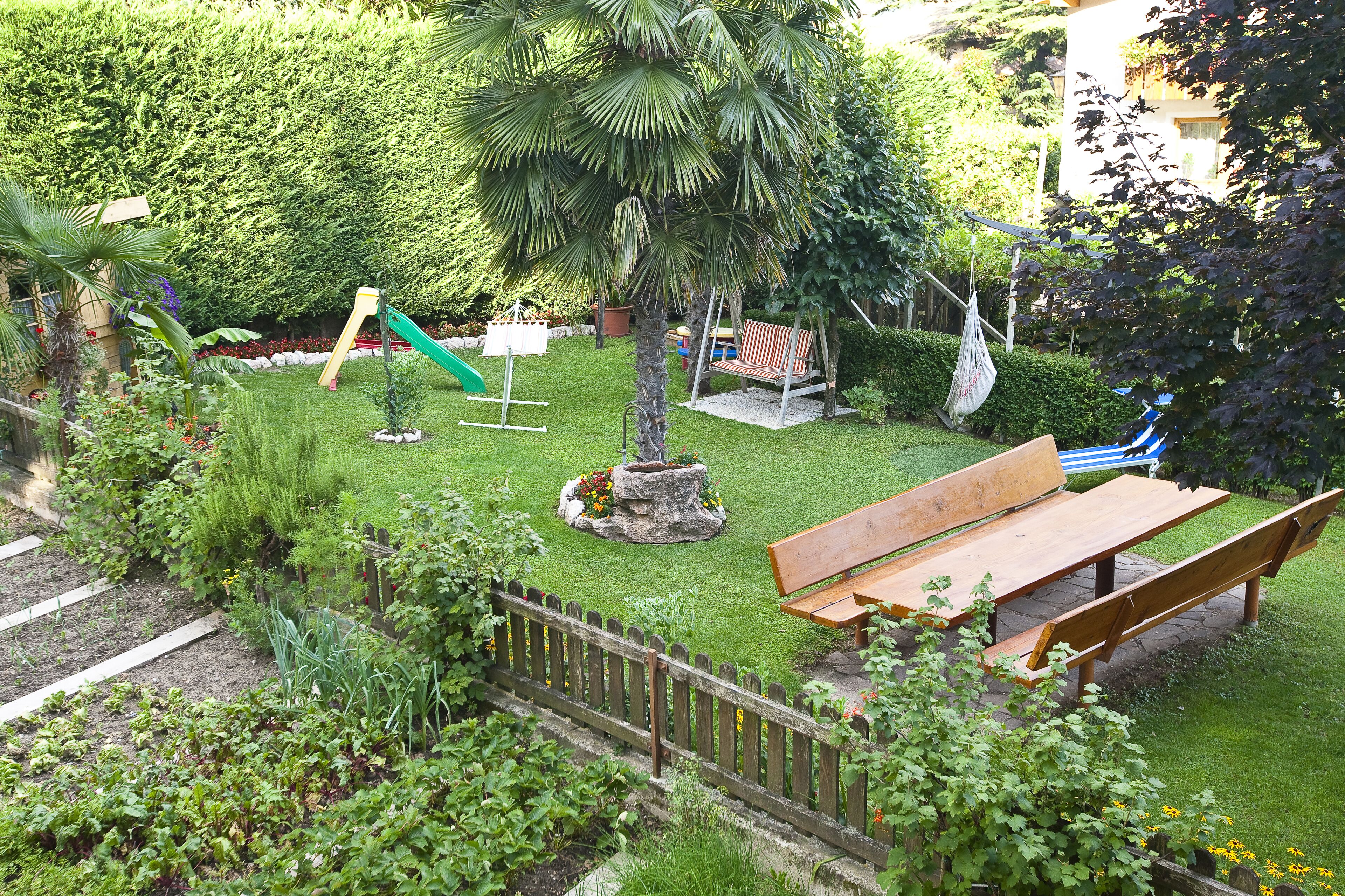 Ein gepflegter Garten mit einer hölzernen Bank, einem kleinen Baum und einem Spielbereich mit einer Rutsche.