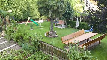 Ein gepflegter Garten mit einer hölzernen Bank, einem kleinen Baum und einem Spielbereich mit einer Rutsche.