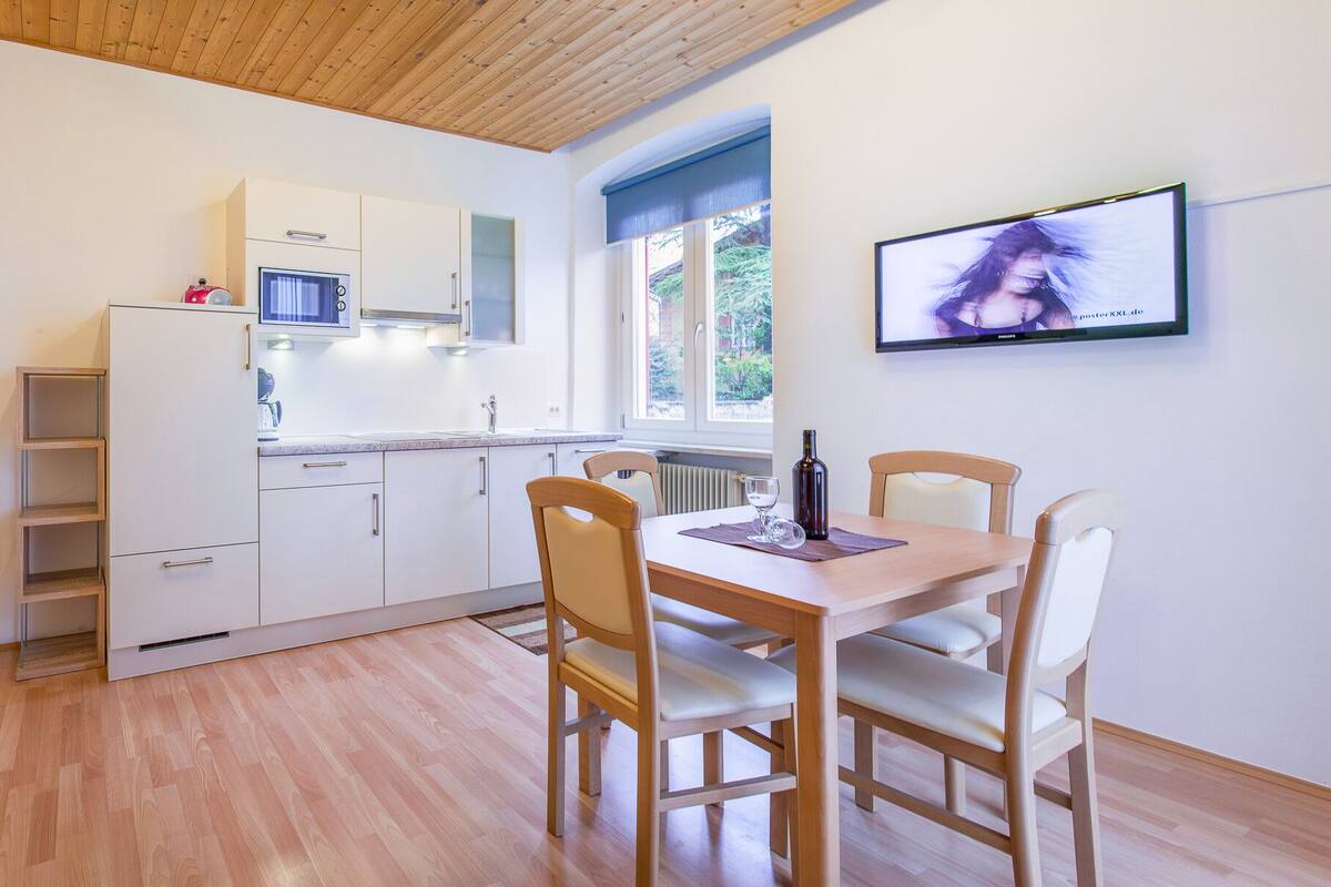 A modern kitchen with white cabinets, a dining table with chairs, and a television mounted on the wall.