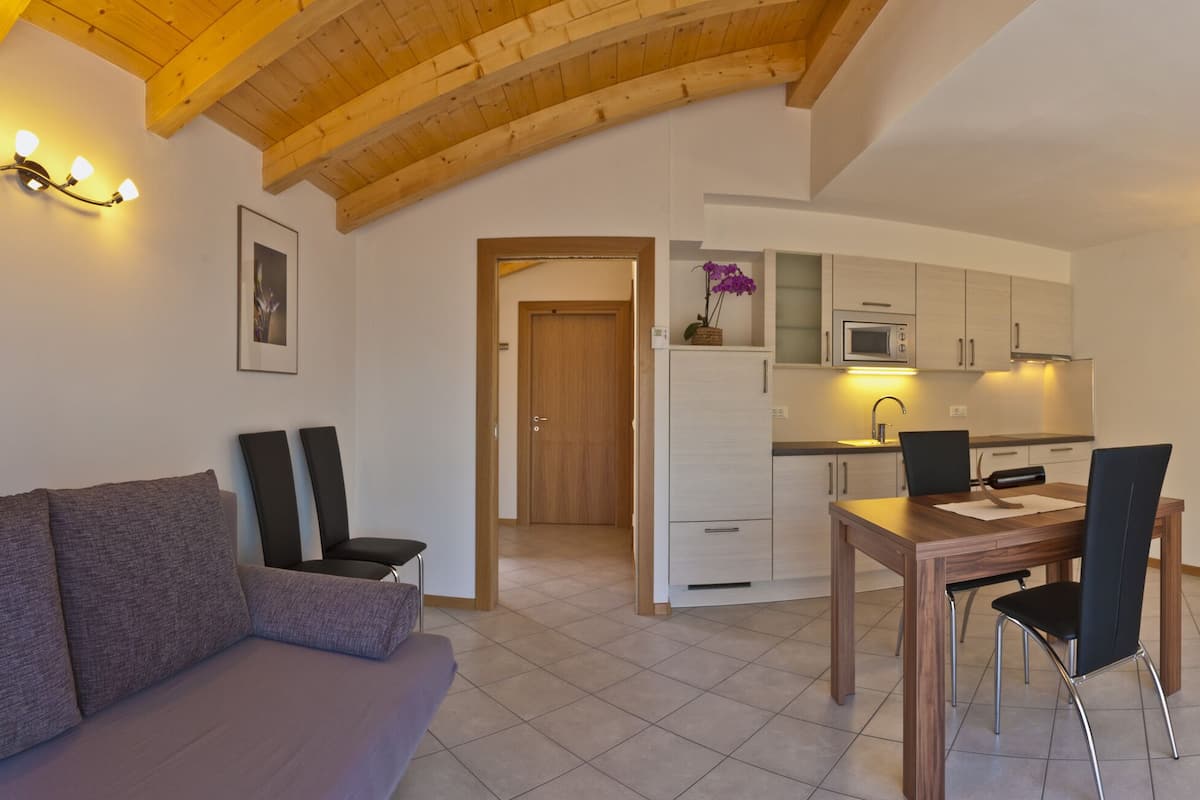 A modern living room with a sofa, a dining table, and chairs. There is a kitchen area with cabinets and a microwave.