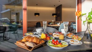 A breakfast table with various dishes, a vase with a flower, and a view of the city through large windows. - Rebenheim Frühstückspension - FEWO (Termeno Sulla Strada del Vino)