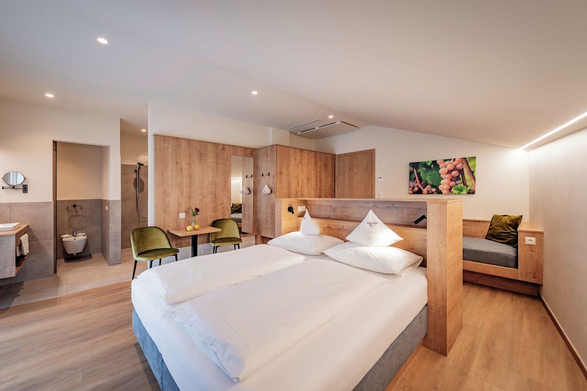 A modern hotel room with a large bed, a wooden headboard, a small desk, and a seating area.