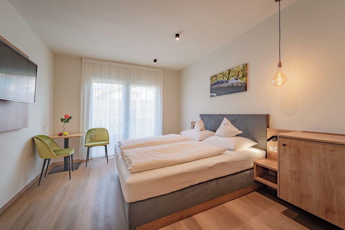 A modern bedroom with a bed, two chairs, a desk, and a TV.