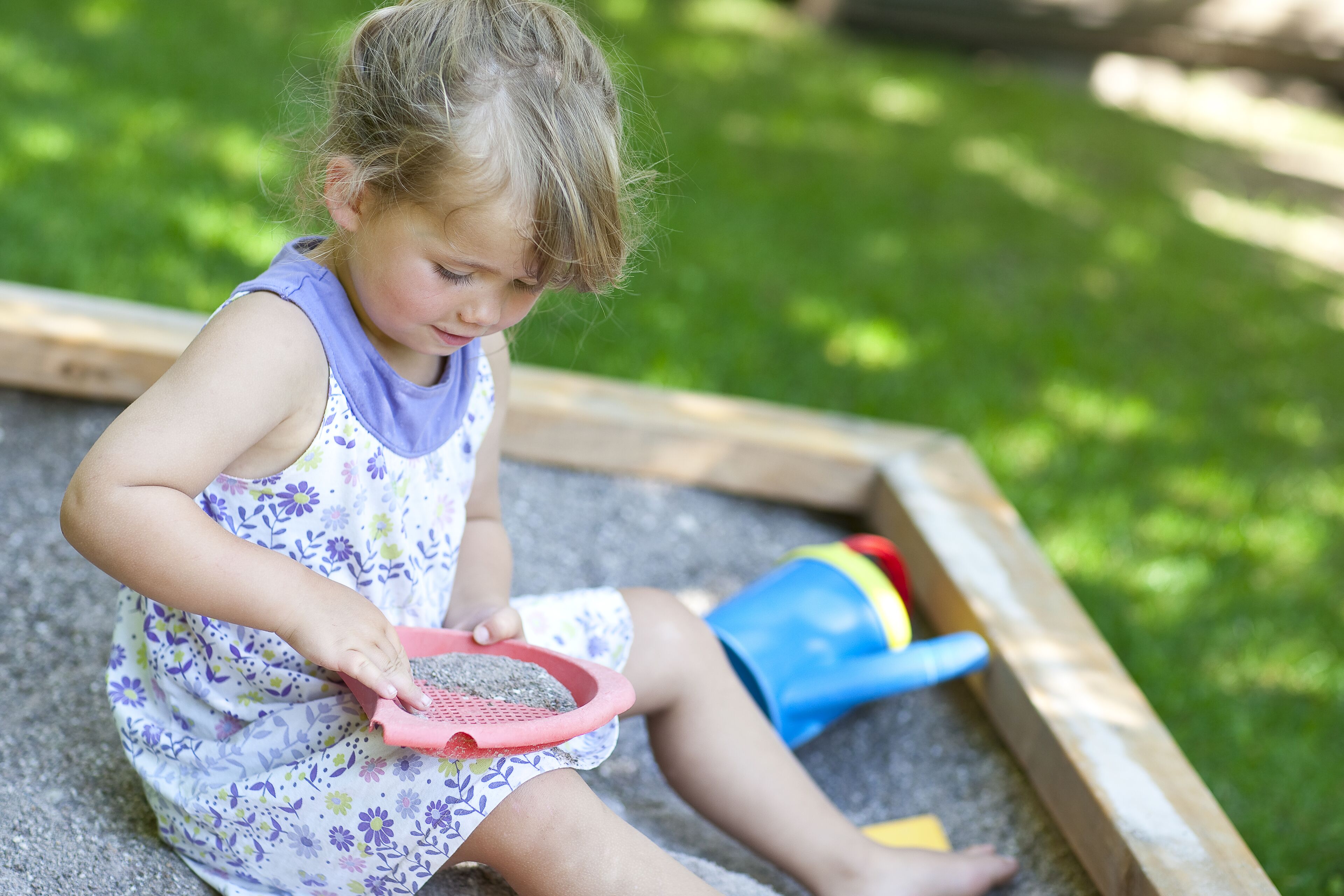 Un bambino gioca con la sabbia in un'area giochi in legno.