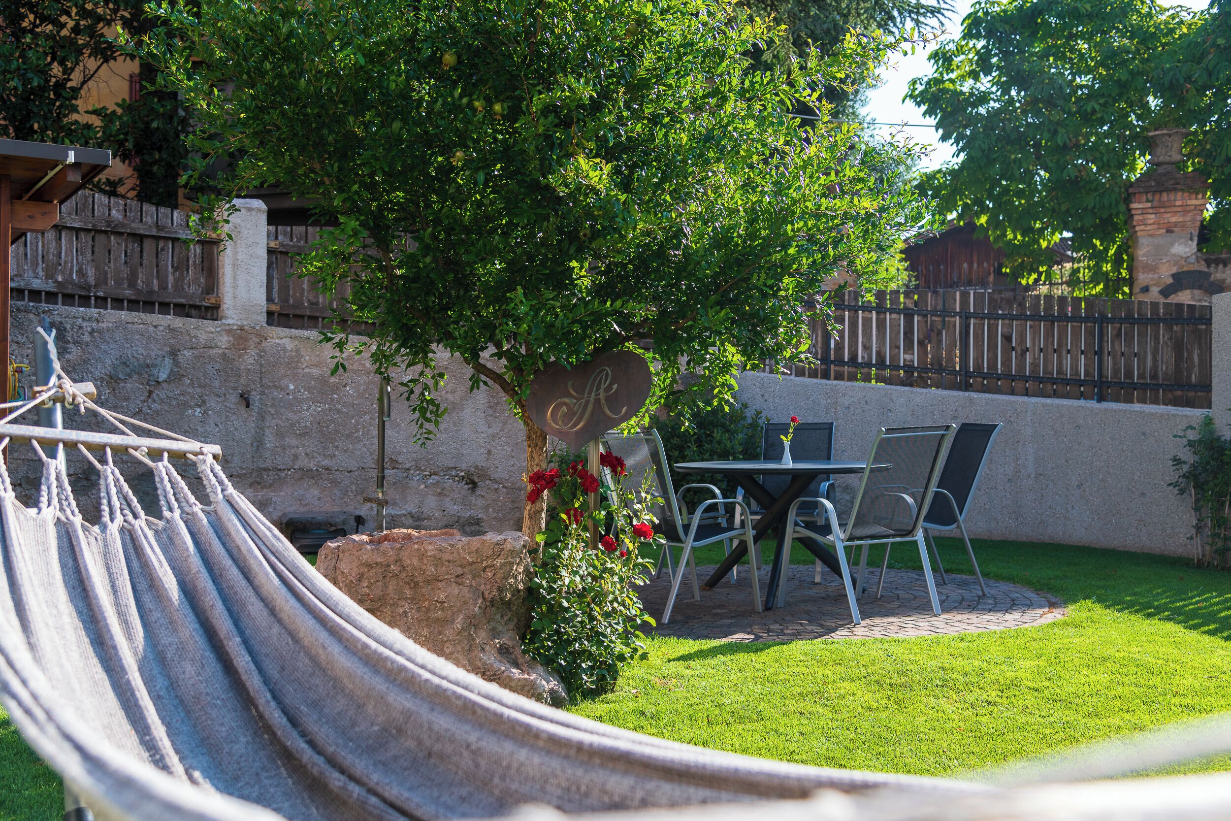 Una hamaca, una mesa con sillas y un pequeño jardín con un árbol y flores.