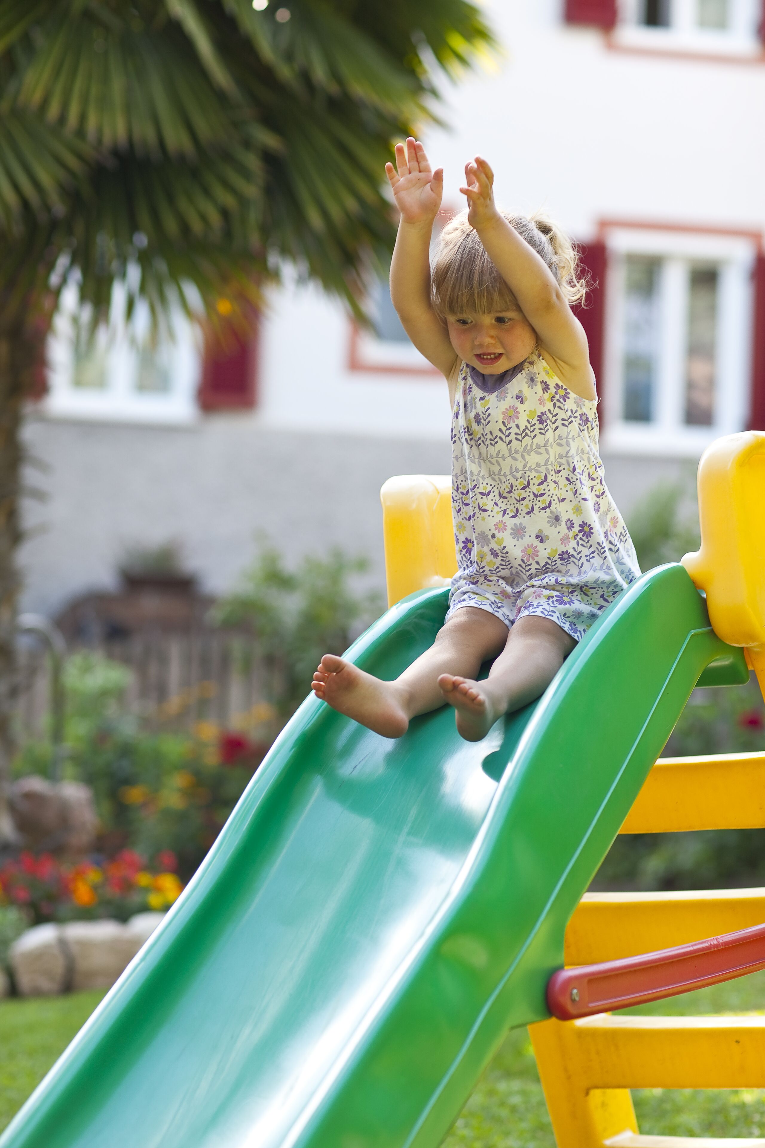 A child on a green slide in a playground with a building in the background.
