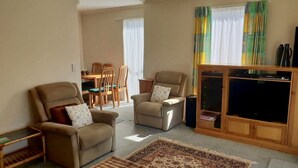 Una sala de estar con dos sillones, un sofá, una mesa de centro, un mueble para televisión con televisor de pantalla plana y una zona de comedor con mesa y sillas.
