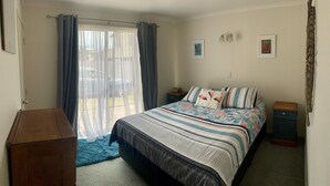 Un dormitorio con una cama, una mesita de noche de madera, una pequeña mesa y una ventana con cortinas.