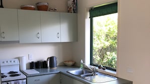 Una cocina con gabinetes blancos, estufa, lavaplatos y ventana con vista a árboles.
