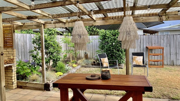 Un patio de madera con una mesa y sillas, rodeado de un jardín y una cerca de madera.