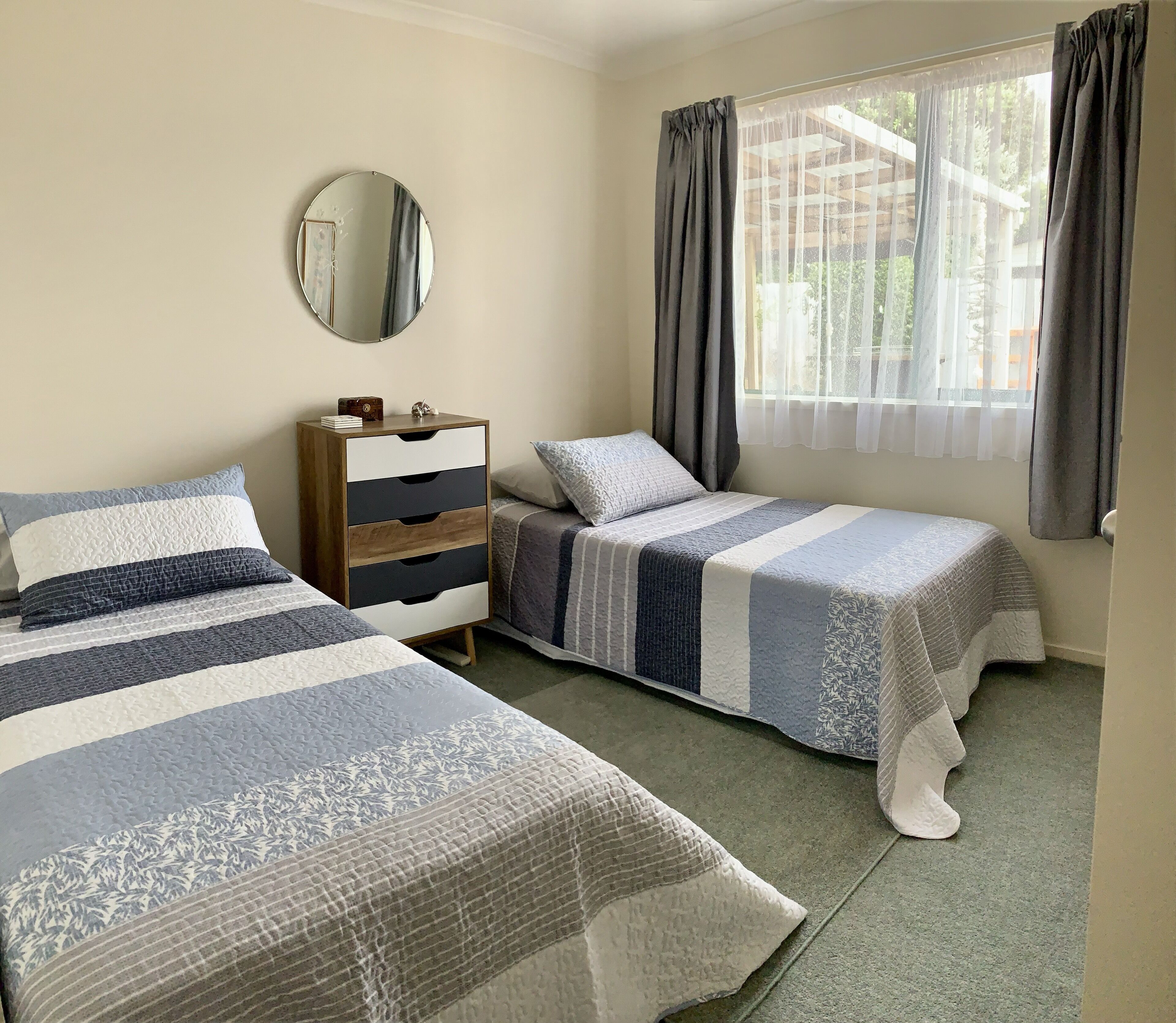 Une chambre avec deux lits, une commode, un miroir et une fenêtre avec des rideaux.