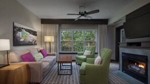 Een moderne woonkamer met een bank, fauteuils, een salontafel, een open haard en een televisie.