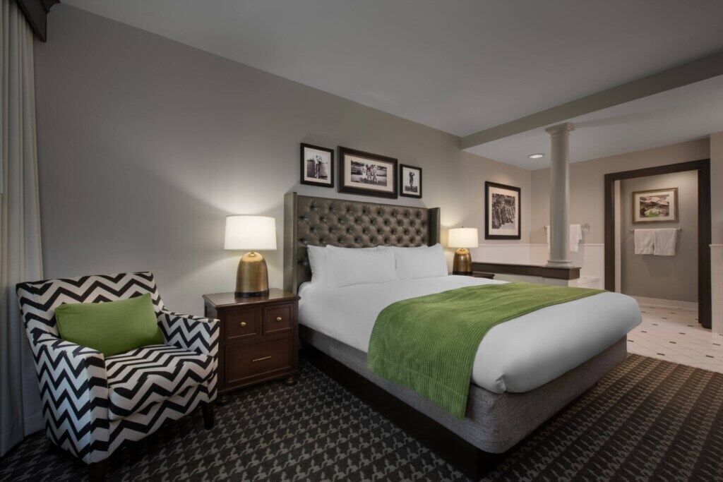 A hotel room with a large bed, a chair, a nightstand, and a picture above the bed.