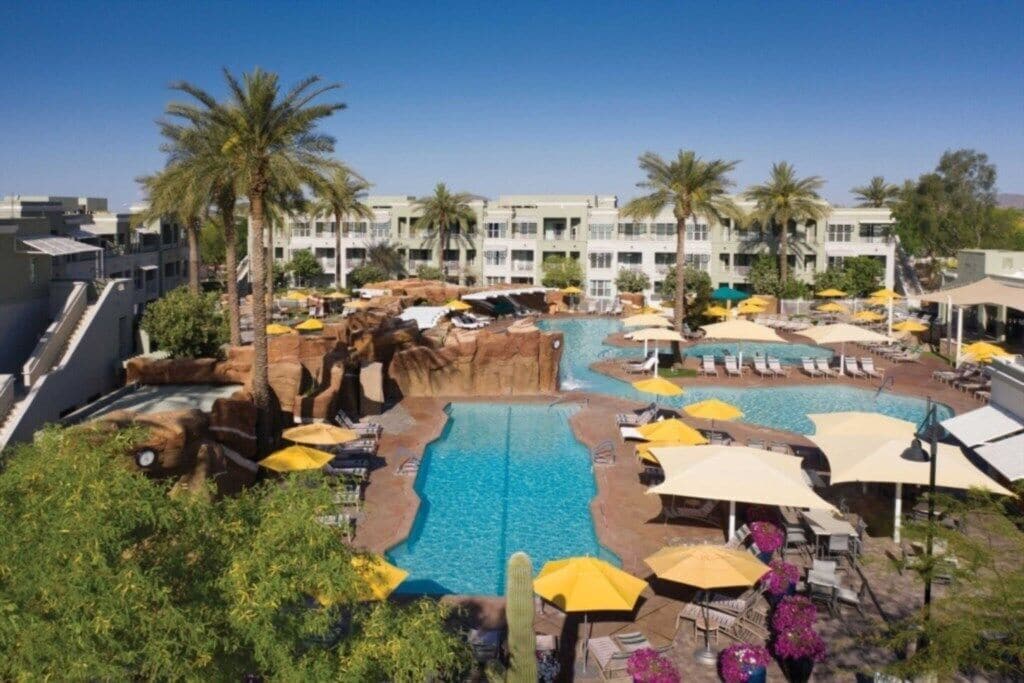 A hotel with a swimming pool, palm trees, and sun loungers.