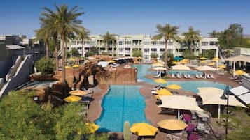 A hotel with a swimming pool, palm trees, and sun loungers.