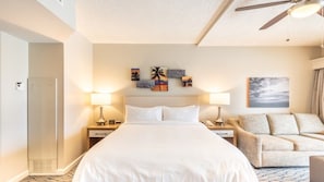 Una camera d'albergo con un letto, due comodini con lampade, un divano, una ventola a soffitto e opere d'arte appese al muro.