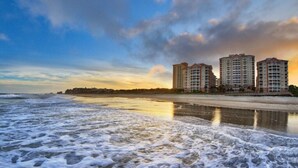 Un hôtel situé en bord de mer, composé de plusieurs immeubles de grande hauteur, avec une plage de sable et des vagues.