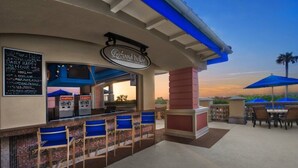 Un espace bar extérieur avec une enseigne indiquant « Sand Dollar Pool Bar », des chaises bleues et des tables avec des parasols.