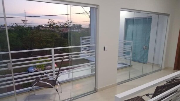 A balcony with a chair, a glass door, and a view of the cityscape. - Recanto do Tanaca Holiday homes (Olímpia)