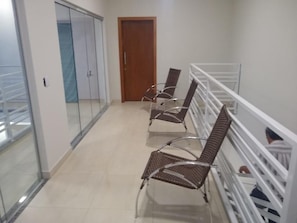 A corridor with a glass wall, a wooden door, and two metal chairs with metal frames.
