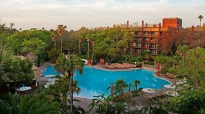 A resort with a large pool surrounded by lush greenery and a multi-story building with balconies.
