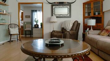 A living room with a round wooden coffee table, a brown leather armchair, a beige sofa, and a wooden cabinet with glass doors.