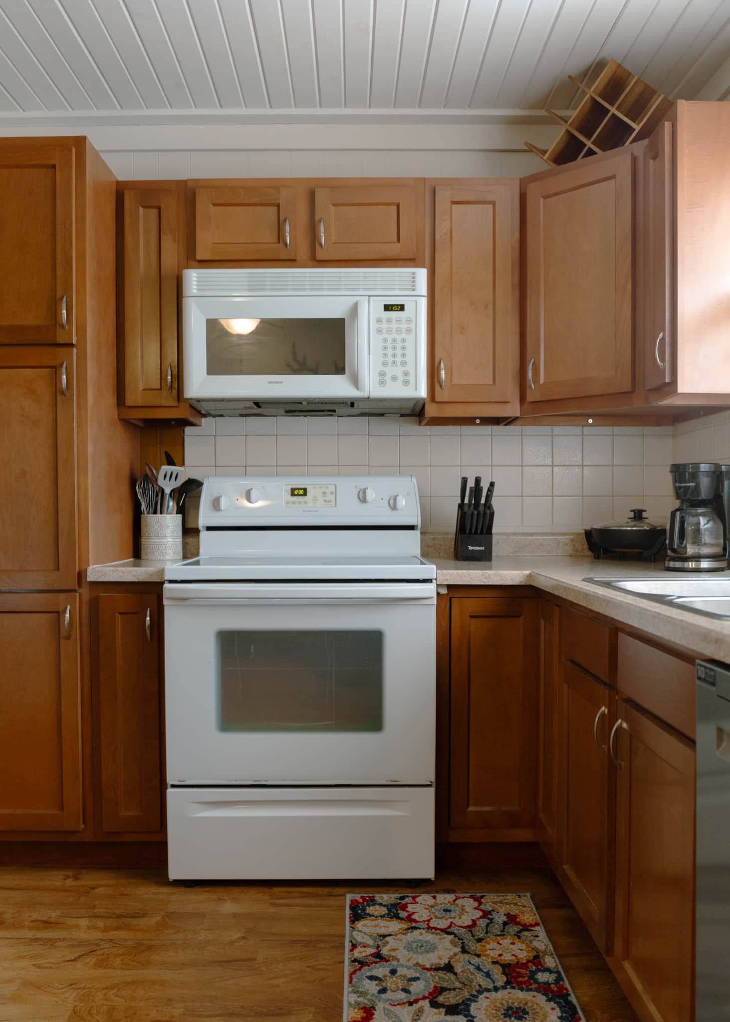 A kitchen with wooden cabinets, a white microwave, a stove, and a coffee maker.
