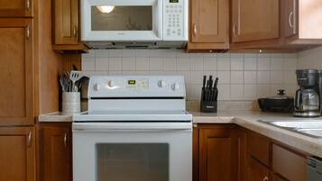 A kitchen with wooden cabinets, a white microwave, a stove, and a coffee maker.