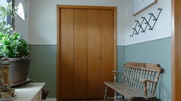 A hallway with a wooden door, a bench, a potted plant, and a wall-mounted sign.