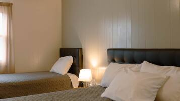 A hotel room with two beds, a nightstand, a lamp, and a window with curtains.