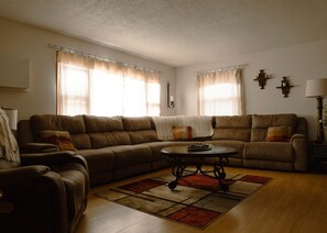 A living room with a brown sectional sofa, a round coffee table, and a patterned rug.