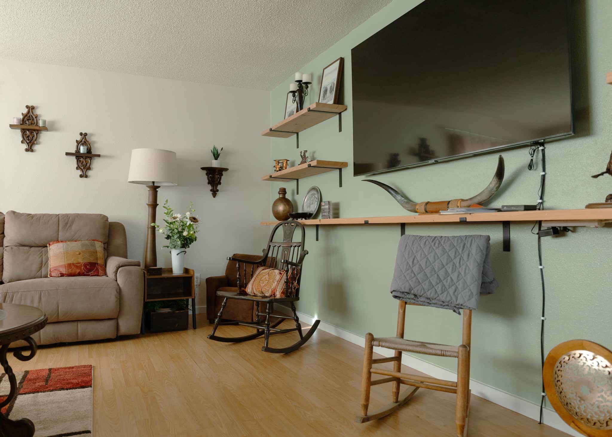 Un salon comprenant un canapé, un fauteuil à bascule, une table et un téléviseur fixé au mur.