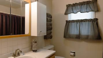 Un baño con lavabo, espejo, inodoro, toallero y ventana con cortinas.