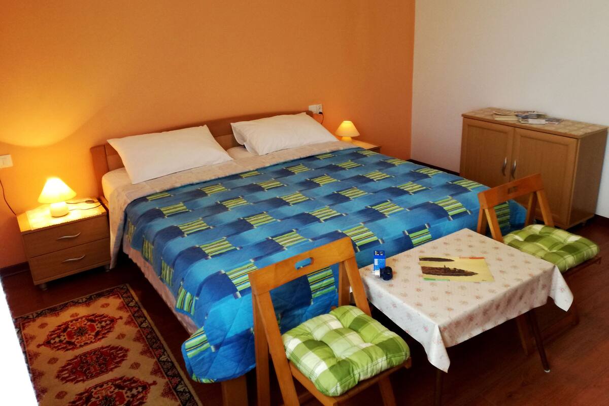 Quarto com cama, mesas de cabeceira, uma mesa, cadeiras e um armário.