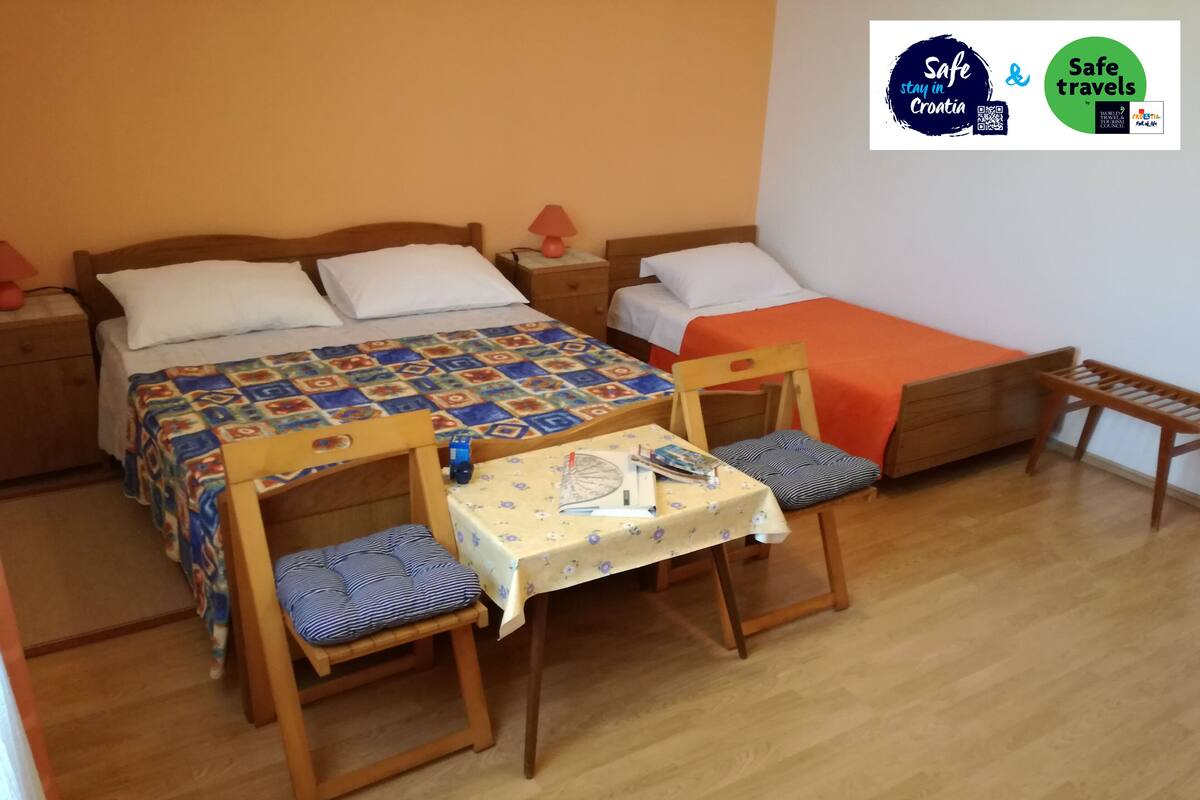 Quarto com duas camas, uma mesa e cadeiras, e um pequeno banco.