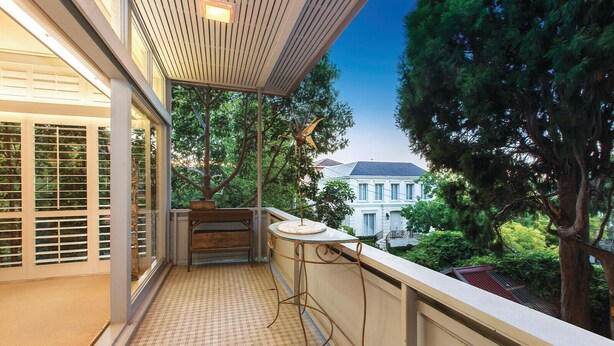 A balcony with a tiled floor, a wooden bench, a small table, and a view of a house and trees. - Toorak Luxury Living (Toorak)