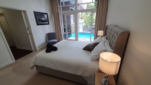 A hotel room with a large bed, a bedside lamp, a chair, a framed picture on the wall, and a view of a swimming pool. - Toorak Luxury Living (Toorak)