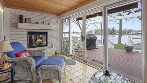 Un salon chaleureux, doté de meubles en osier, d’une cheminée et de grandes fenêtres donnant sur une terrasse et un lac.