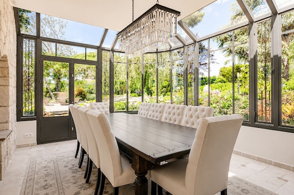 A conservatory with a dining table and chairs, large windows, and a hanging light fixture.