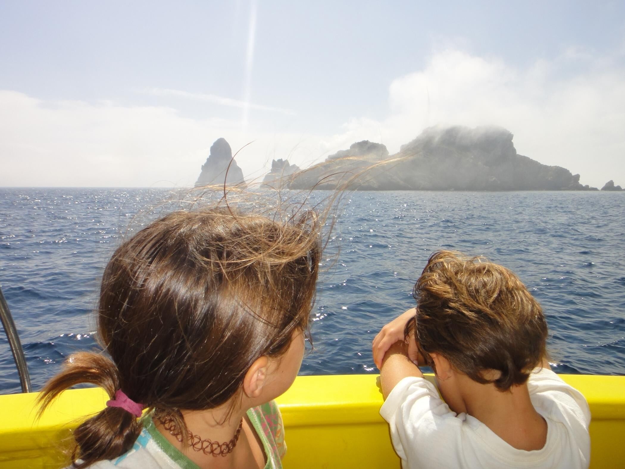 Deux enfants se trouvent sur un bateau, et on aperçoit, au loin, une île rocheuse.