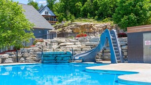 Una piscina con tobogán, rodeada de muros de piedra y una cubierta de madera.