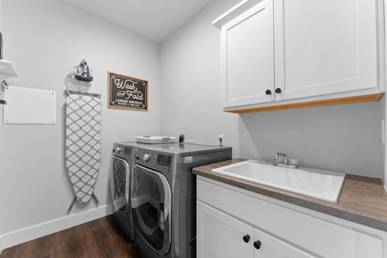 A laundry room with a washing machine, dryer, and a sink. There is a sign on the wall that says "Wash and Fold Laundry Service Co."