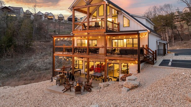 Una casa de madera de varios pisos con balcón, zona de estar exterior y luces colgantes.