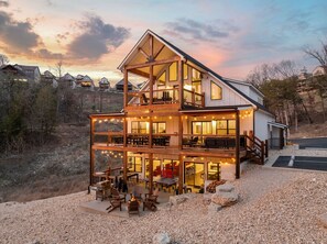 Una casa de madera de varios pisos con balcón, zona de estar exterior y luces colgantes.