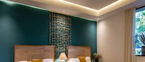 Una habitación de hotel moderna con dos camas, un tapiz decorativo, una mesita de noche con lámpara y una ventana con cortinas.
