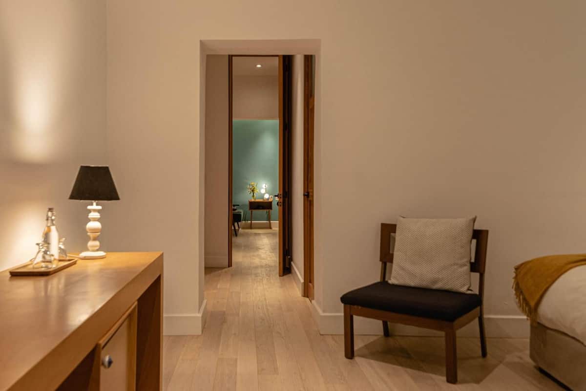 A hotel room with a wooden desk, a chair, a bed, and a view into the adjacent room.