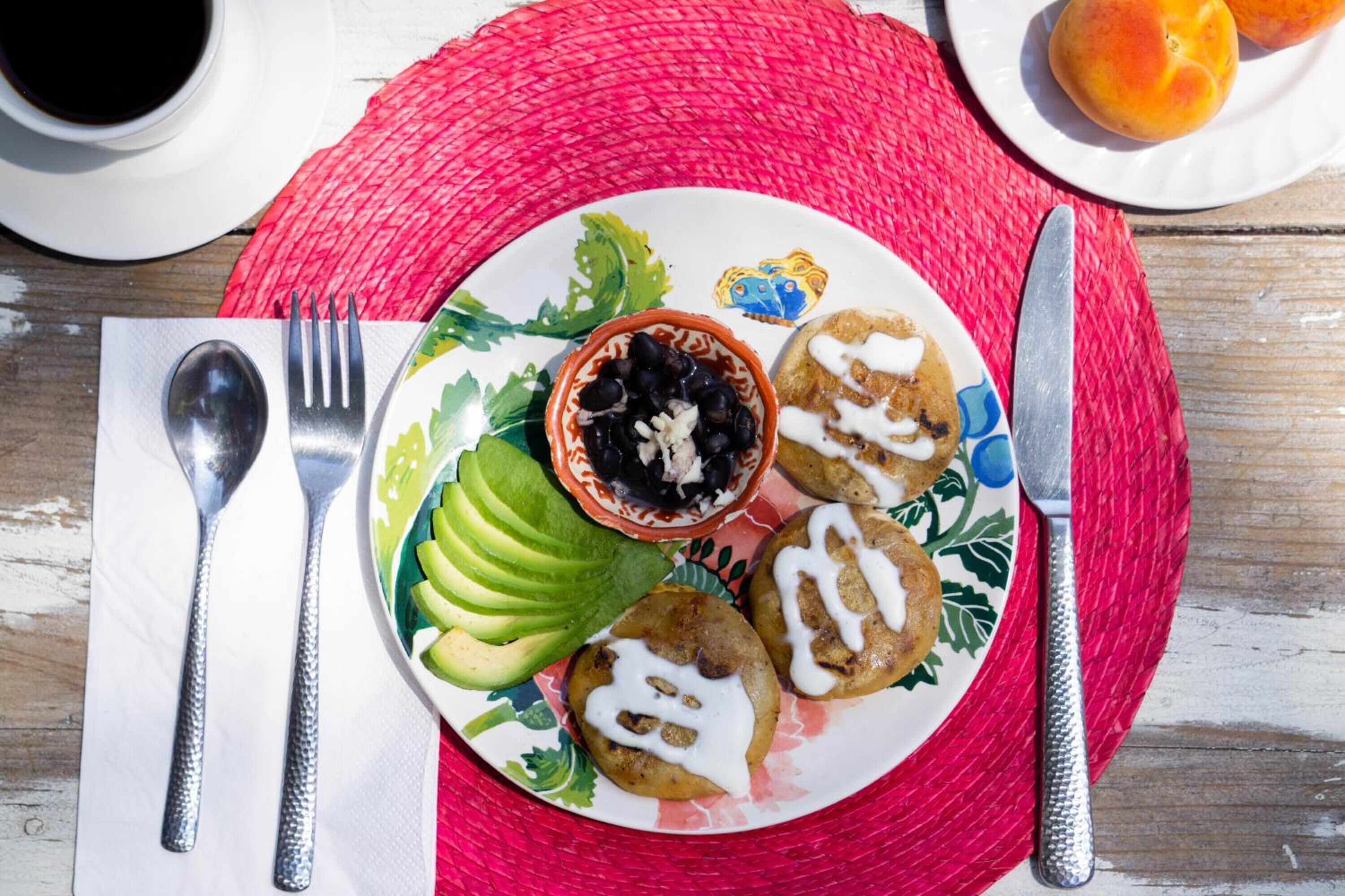 A plate with food items, a fork, a knife, and a cup on a table with a red placemat.