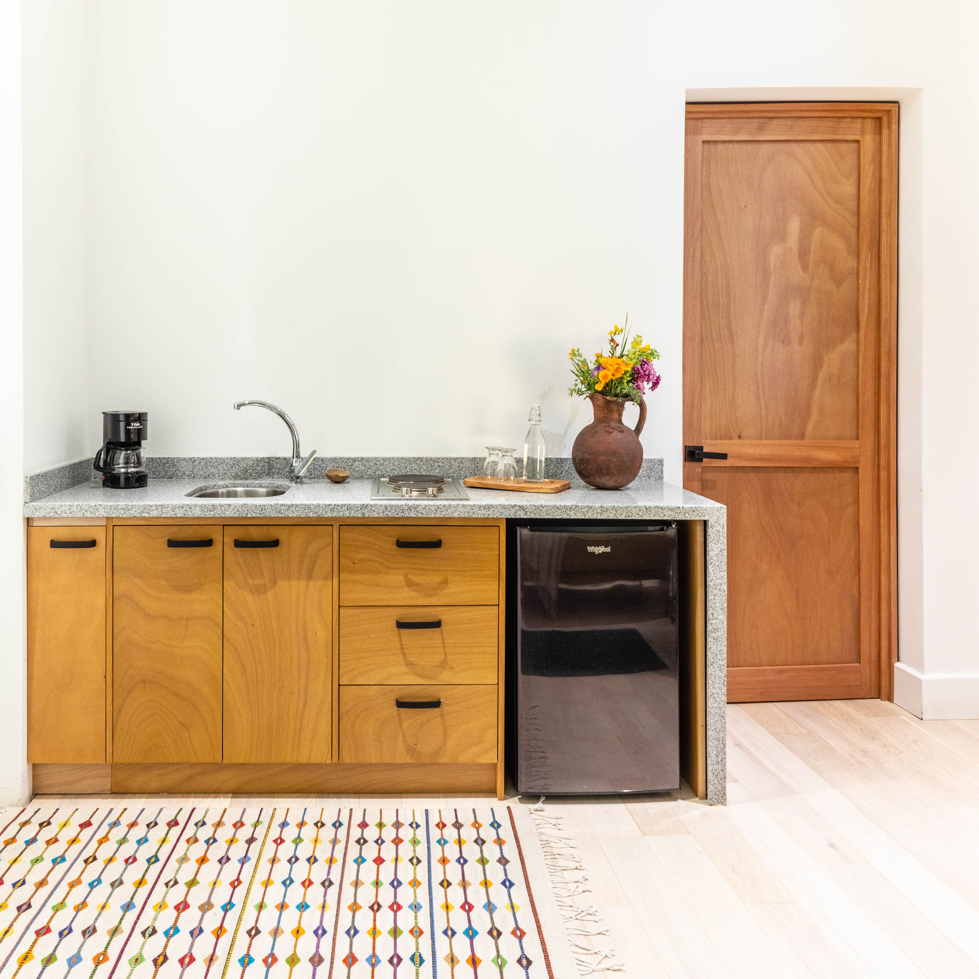 A kitchen with wooden cabinets, a dishwasher, a coffee maker, a vase with flowers, and a door.