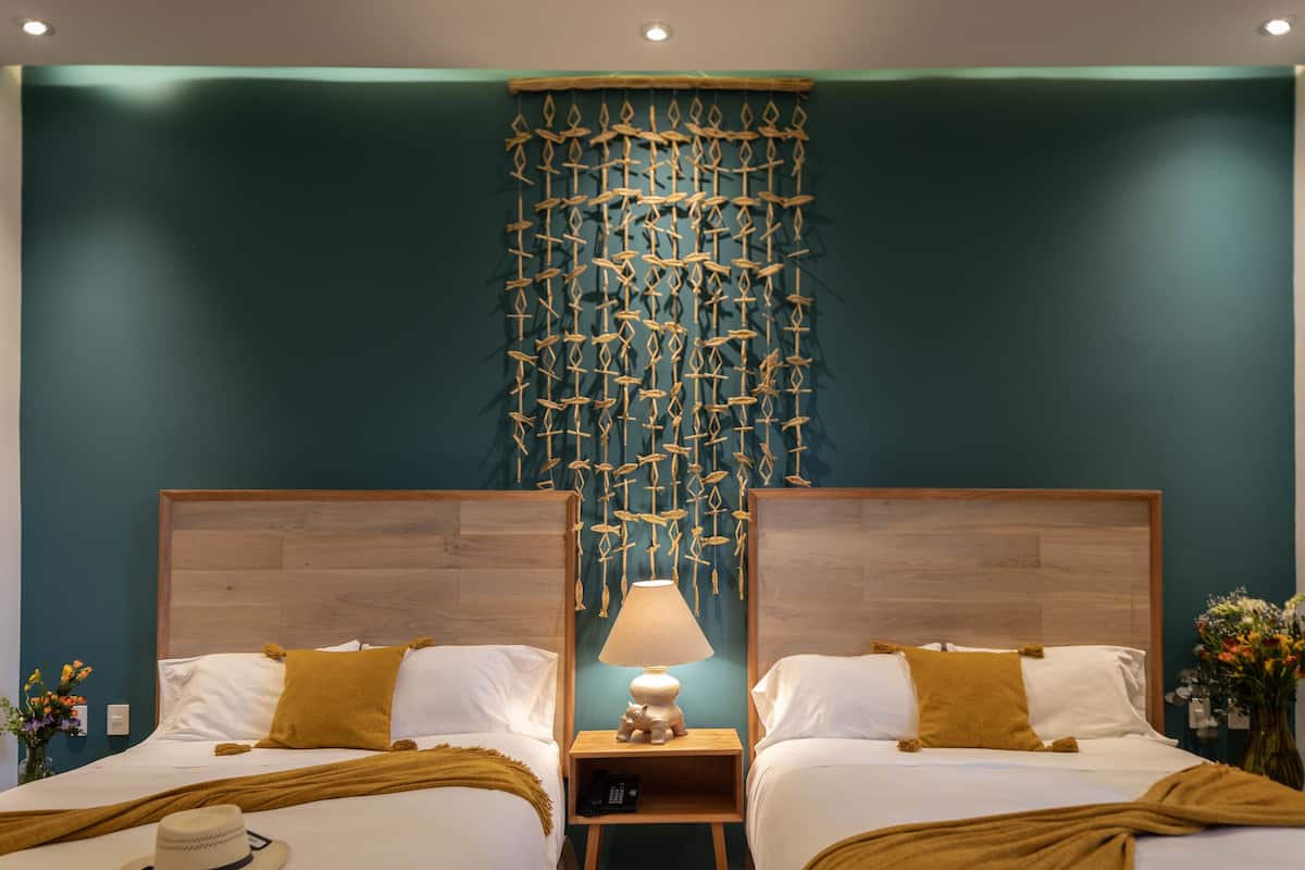 A hotel room with two beds, a wooden headboard, a wall hanging, and a nightstand with a lamp.