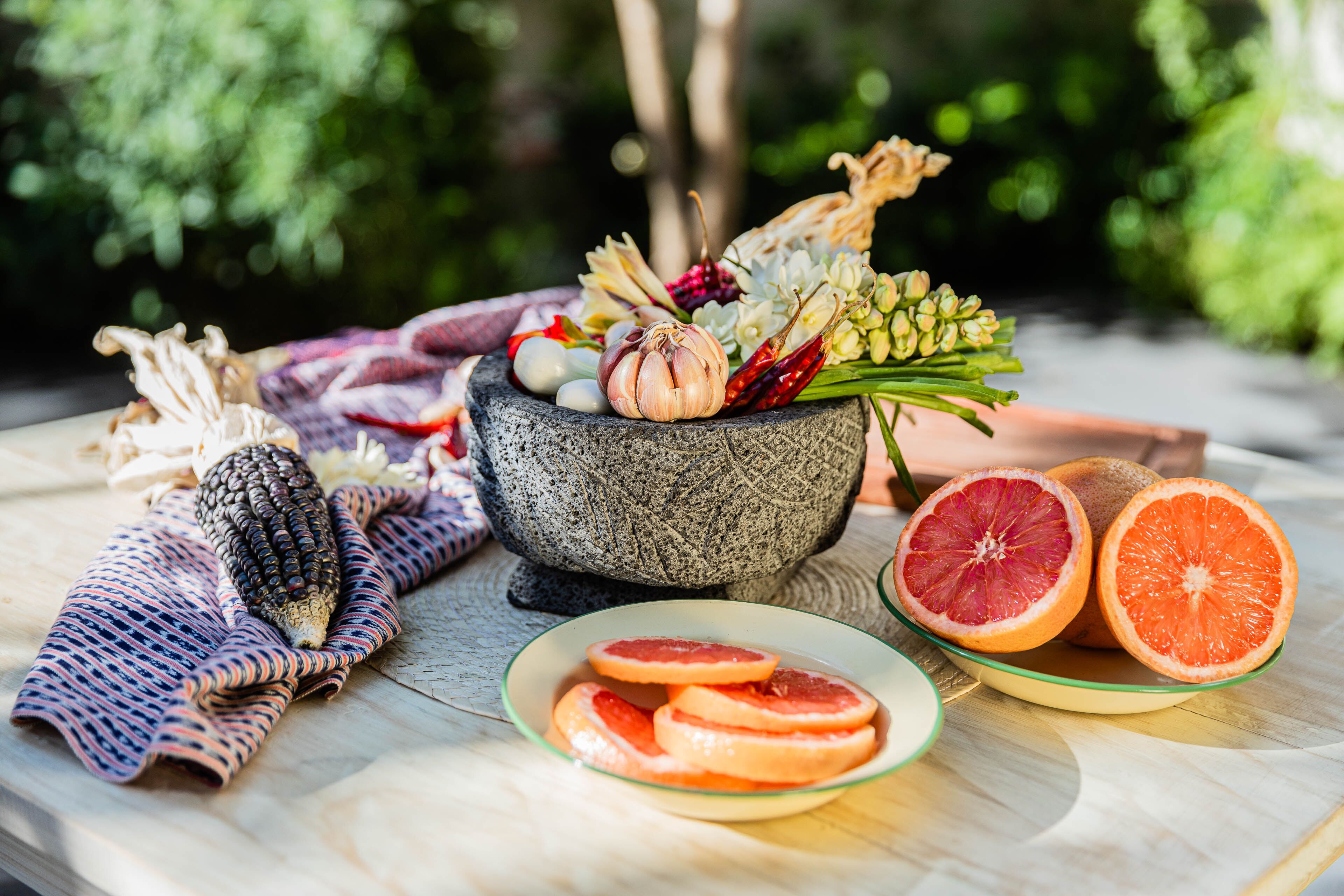 A stone mortar with various herbs and spices, a cloth, and a plate with grapefruit slices.